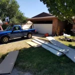 blue trucks in a driveway replacing garage door panels. Garage door panels laid out on front lawn.