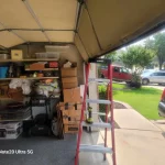 a red ladder holding up a broken garage door. A Garage full of objects being stored on shelves.