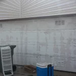 Completed garage door repair. White garage door with garbage and cooler in front of it.